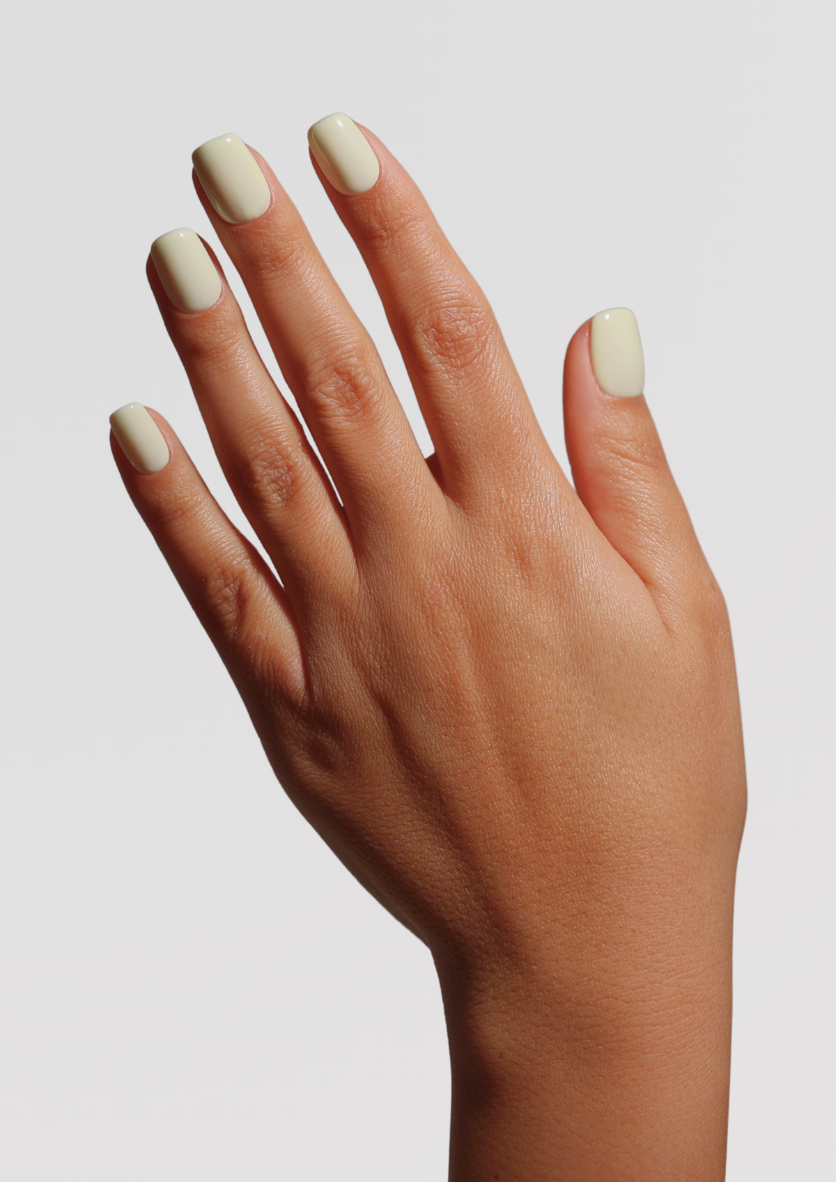 A hand with short, rounded nails painted in a glossy off-white cream shade, shown against a light gray background.